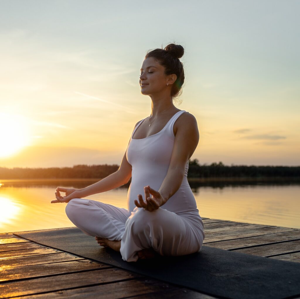 Pregnant woman doing yoga at lake during sunset.